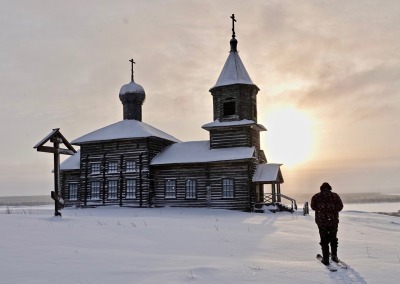 Man approaching the wooden church in Bolshaya Nisogora village on skis, Leshukonskoye District